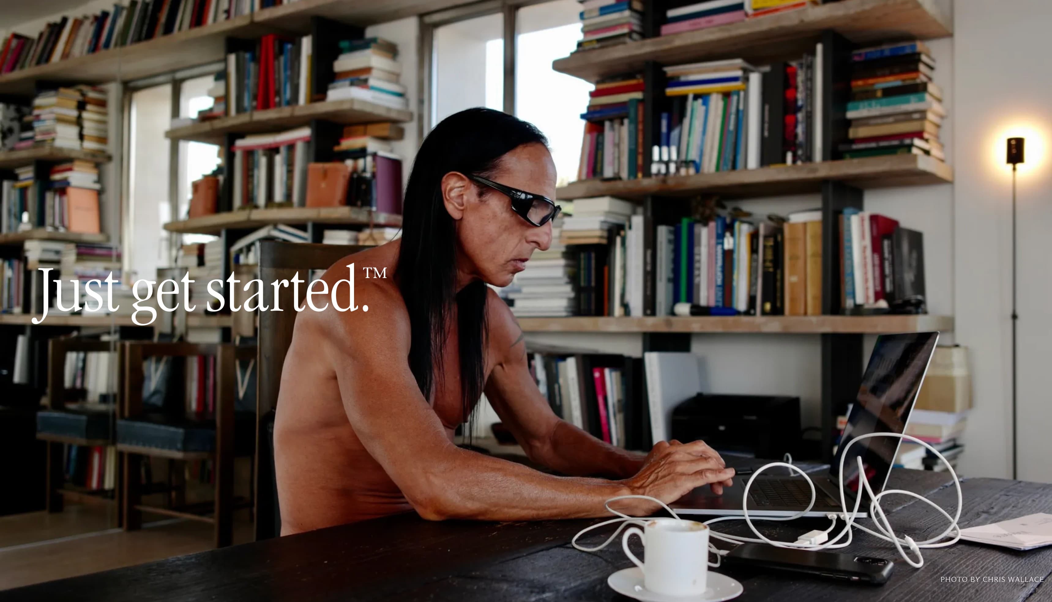Just get started. A maker at work on a laptop, in front of a wall of books.